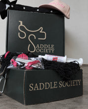 Saddle Society box with a black pearl-snap shirt, pink Classic Cowboy cap, pink and black hay net, and supplement