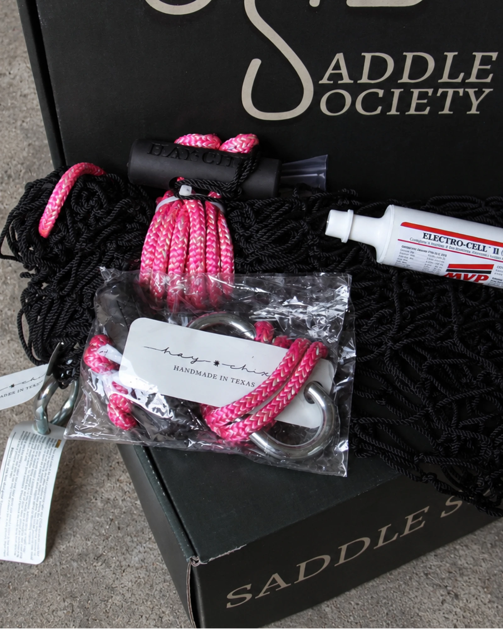Close-up of a hay net with pink rope and a paste syringe on a Saddle Society box