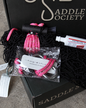 Close-up of a hay net with pink rope and a paste syringe on a Saddle Society box